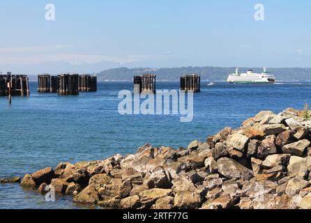 Con un molo di roccia in primo piano, un iconico traghetto bianco dello stato di Washington si allontana dagli Edmonds, il molo di Washington, mentre attraversa Puget Sound Foto Stock