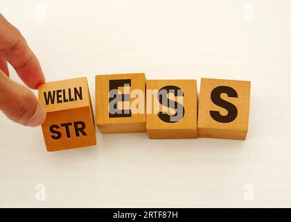 Benessere invece dello stress. La mano trasforma un cubo e cambia la parola "stress" in "benessere" su sfondo bianco. Concetto. Copia spazio. Foto Stock