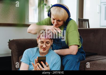 Figlia con smartphone che insegna alla madre anziana sicurezza informatica, shopping online Foto Stock