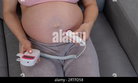 Primo piano della pancia di una donna incinta usando un doppler domestico. Schermo vuoto. Foto Stock