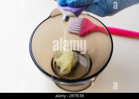 ragazza con guanti protettivi in gomma blu che tiene una spazzola tra le mani e mescola la tintura per capelli primo piano cura dei capelli a casa. Foto Stock