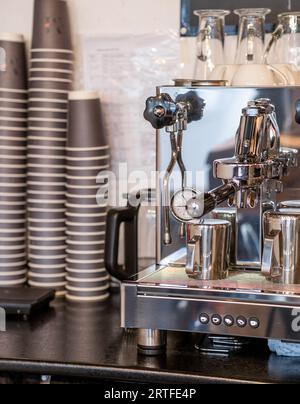 Il barista prepara caffè fresco nella macchina del caffè la mattina nel caffè. Ci sono delle tazze di caffè sul tavolo per i clienti. Macchina da caffè c Foto Stock