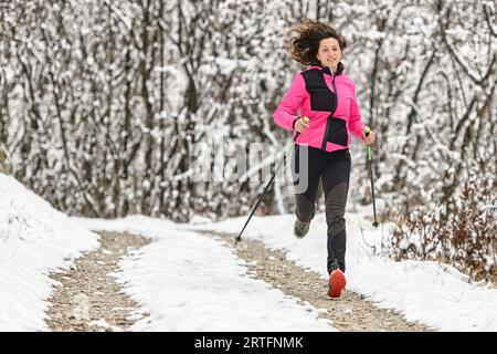 La ragazza corre con i bastoncini in mano su strada sterrata in inverno Foto Stock