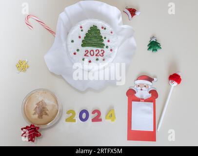 Foto concettuale della pagina del calendario di dicembre per il nuovo anno 2024. Passare dal 2023 al 2024. Sul tavolo c'è una torta, una tazza di caffè, varie vacanze così Foto Stock