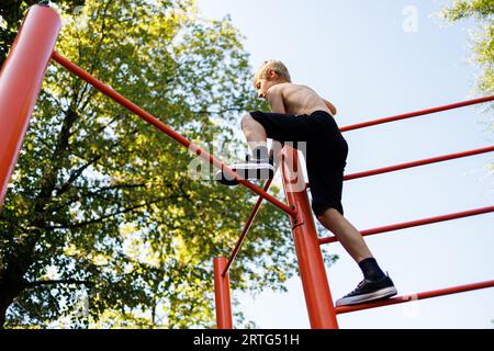 Vista dal basso di un adolescente che sale su un bar di ginnastica. Allenati in strada su un bar orizzontale nel parco scolastico. Foto Stock