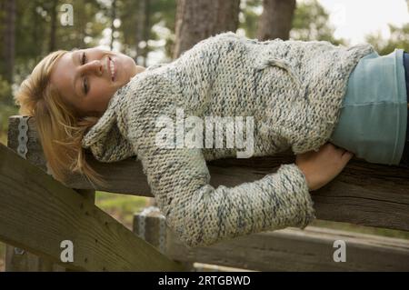 Giovane donna sdraiata su una trave di legno sorridente Foto Stock