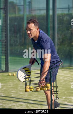 Uomo attivo in abbigliamento sportivo con racchetta in mano che prende la palla mentre gioca a padel nel parco giochi nelle soleggiate giornate estive Foto Stock