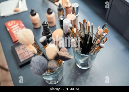 Dall'alto, collezione di varie spazzole cosmetiche in bicchieri collocati sul tavolo con prodotti per il trucco assortiti in un moderno salone di bellezza Foto Stock