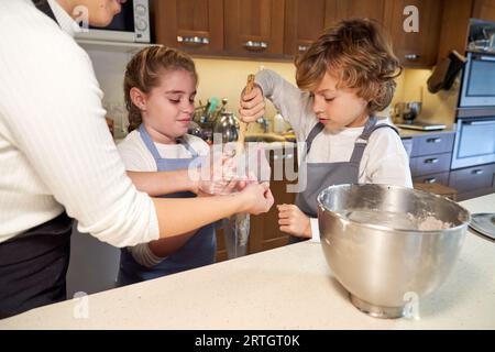 Coltiva la madre che aiuta a frustare i grembiuli per mettere la panna dolce nel sacchetto della pasticceria mentre i cupcake vengono cotti insieme in cucina Foto Stock