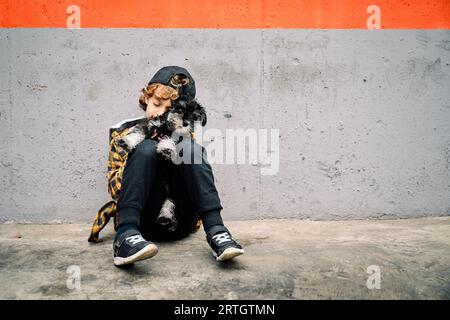 Un bambino seduto da solo sul marciapiede vicino a un muro di cemento e dormiva tranquillamente con il cane sulle ginocchia Foto Stock