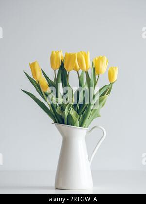 Bouquet di tulipani gialli vividi disposti in vaso di ceramica sul tavolo contro la parete bianca dello studio Foto Stock