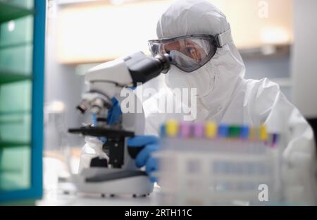 Scienziato in un abito protettivo che guarda attraverso un microscopio in un moderno laboratorio attrezzato Foto Stock