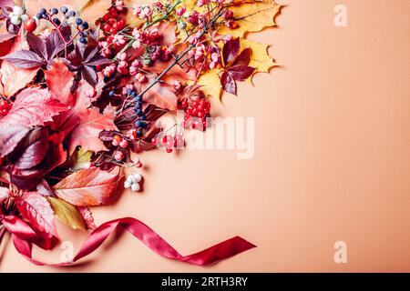 Bouquet autunnale di foglie di arancia gialla e frutti di bosco disposti su fondo marrone con nastro. Decorazioni autunnali. Spazio Foto Stock