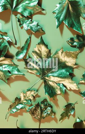 Immagine verticale di foglie autunnali in oro metallico che giacciono su sfondo arancione Foto Stock