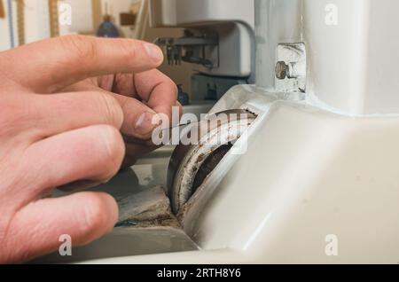 Un uomo affina un ago metallico su una mola. Primo piano della mano del padrone Foto Stock