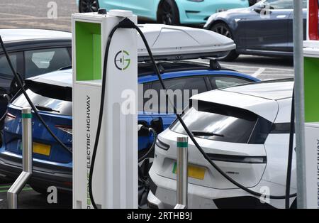Ricarica di un veicolo elettrico bianco o di un veicolo elettrico presso una stazione di servizio su un percorso principale nel sud-ovest dell'Inghilterra Foto Stock
