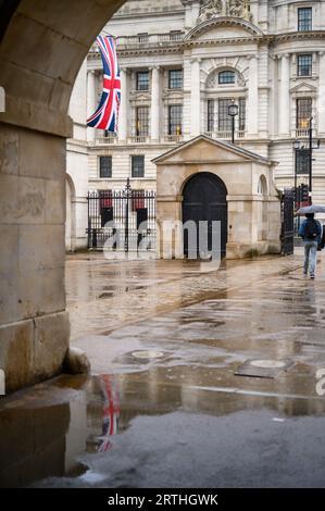 LONDRA - 24 aprile 2023: Una bandiera Union Jack che si riflette elegantemente nelle pozzanghere sul terreno pavimentato sotto l'arco alla Horse Guards Parade. Foto Stock