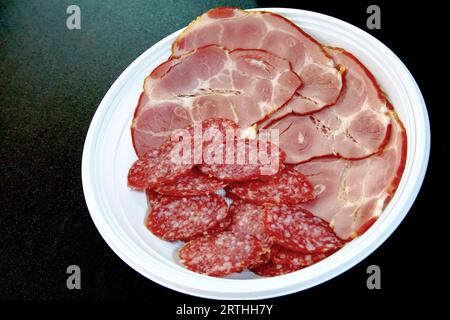 Salame affumicato, peperoni e fette di prosciutto, in un piatto di plastica usa e getta Foto Stock