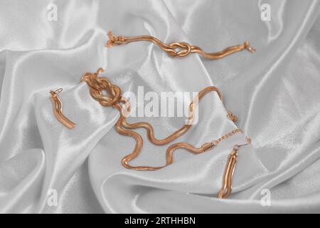 collana e orecchini da donna in oro su sfondo di seta grigia Foto Stock