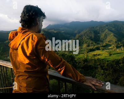 Vista posteriore del tranquillo viaggiatore maschile in piedi in un balcone mentre cammina in montagna con il tempo nuvoloso di giorno, Colombia Foto Stock