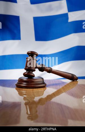 Martelletto di legno di mogano su un tavolo di legno lucido, bandiera della Grecia sullo sfondo Foto Stock