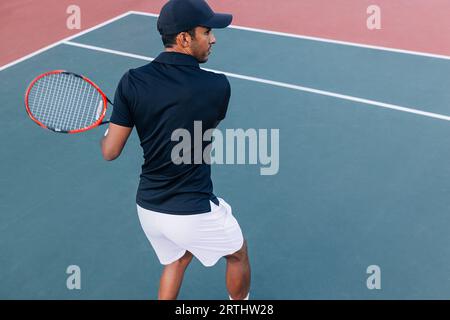 Vista posteriore di un tennista maschile che pratica un campo duro all'aperto Foto Stock