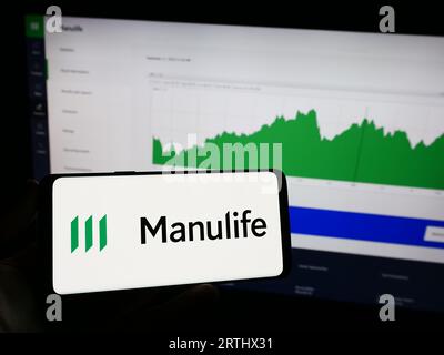 Persona che possiede il cellulare con il logo della società canadese Manulife Financial Corporation sullo schermo davanti alla pagina Web. Concentrarsi sul display del telefono. Foto Stock
