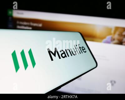 Smartphone con logo della società canadese Manulife Financial Corporation sullo schermo di fronte al sito Web. Mettere a fuoco il display centrale sinistro del telefono. Foto Stock