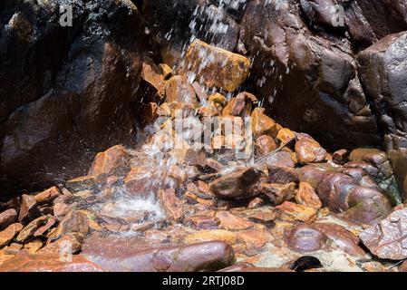 Una piccola cascata tra rocce e pietre in moss da spiaggia Foto Stock