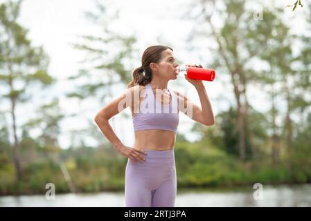 Donna sportiva che beve acqua da una bottiglia di vetro dopo l'esercizio, parte della serie. Foto Stock