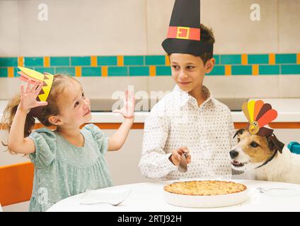 Ragazza carina che mostra quanto dovrebbe essere grande il suo pezzo di torta di mele del Ringraziamento. Bambini che indossano cappelli da festa che mangiano una torta di Natale Foto Stock