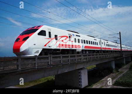 Un moderno treno passeggeri rosso e bianco si dirige su un ponte di legno, offrendo una vista panoramica del paesaggio circostante Foto Stock