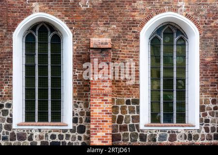 Due finestre ad arco con barre di metallo e bordature bianche su un vecchio muro di mattoni rossi. Dalla serie Windows of the World. Foto Stock