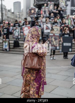 Una donna musulmana si ferma per scattare una foto del manifestante contro il regime iraniano sui gradini di Piccadilly Circus a Londra. Foto Stock