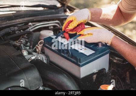 il meccanico automatico ripara un'auto. Un meccanico rimuove la batteria della vettura dalla scatola. Foto Stock