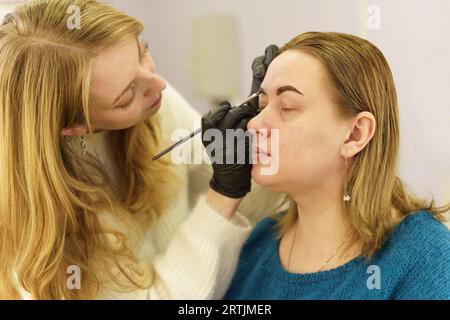 Il master disegna la forma delle sopracciglia con vernice bianca prima della correzione delle sopracciglia. Industria della bellezza. Foto Stock