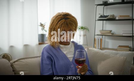 Afro-americano pensive Woman etnico pensiero premuroso ragazza perplessa triste turbata solitaria donna pensare a casa divano con vino rosso messo bicchiere su Foto Stock