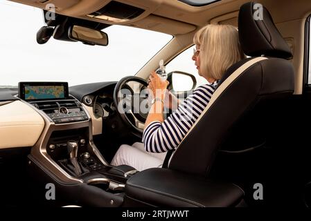 Portsmouth, Inghilterra, Regno Unito. 29 agosto 2023. Donna autista che prende una bevanda d'acqua da una bottiglia di plastica durante un riposo dopo aver guidato la sua auto di lusso. Foto Stock