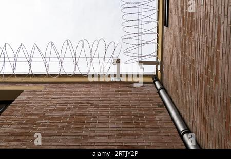 Mura della prigione con barre sulle finestre circondate da filo spinato Foto Stock