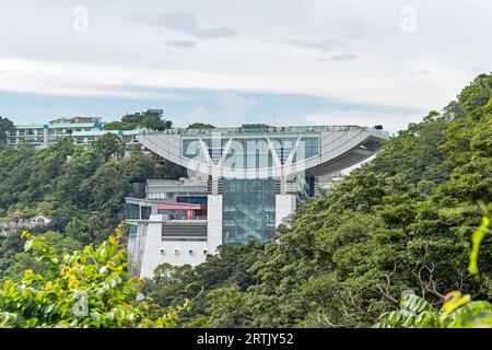 La torre di osservazione Peak sul Victoria Peak in una giornata nuvolosa circondata da alberi. Hong Kong - 27 agosto 2023 Foto Stock