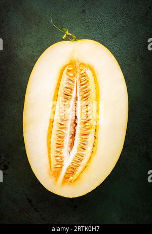 Melone ovale grande, metà tagliata con semi su sfondo verde nero, vista dall'alto Foto Stock