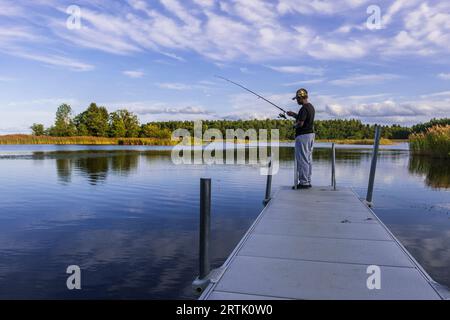 Una donna si trova su un molo e pesca una serata tranquilla e bella nell'arcipelago svedese Foto Stock