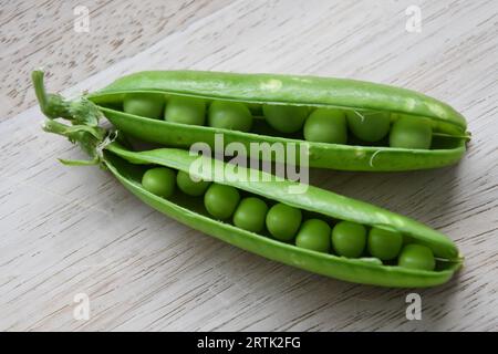 Due fresche cialde di piselli da giardino (Pisum sativum), isolate su uno sfondo di legno. Cibo sano dal giardino. Orientamento orizzontale. Foto Stock