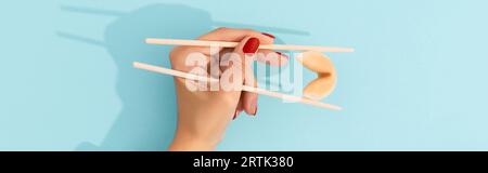 Biscotti di fortuna di tenuta della mano femminile con i chopsticks cinesi su sfondo blu Foto Stock