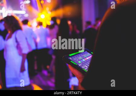 Visione del tecnico dell'illuminazione con tablet, dell'operatore che controlla il suono e la luce durante un concerto dal vivo durante la trasmissione dello spettacolo sul palco, del tecnico con profe Foto Stock