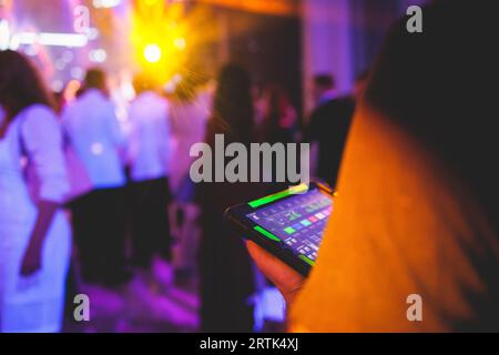 Visione del tecnico dell'illuminazione con tablet, dell'operatore che controlla il suono e la luce durante un concerto dal vivo durante la trasmissione dello spettacolo sul palco, del tecnico con profe Foto Stock