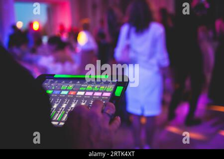 Visione del tecnico dell'illuminazione con tablet, dell'operatore che controlla il suono e la luce durante un concerto dal vivo durante la trasmissione dello spettacolo sul palco, del tecnico con profe Foto Stock