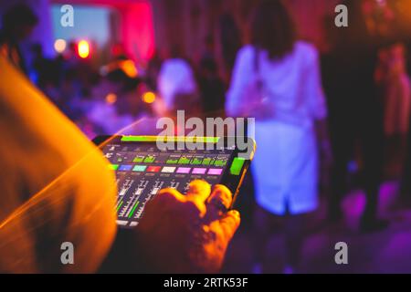 Visione del tecnico dell'illuminazione con tablet, dell'operatore che controlla il suono e la luce durante un concerto dal vivo durante la trasmissione dello spettacolo sul palco, del tecnico con profe Foto Stock