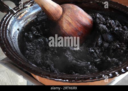 Preparazione della talpa rossa, un tipico piatto messicano in una pentola di argilla con un gigantesco cucchiaio di legno sul fuoco di una stufa con tutti gli ingredienti integrati Foto Stock