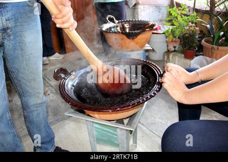 Preparazione della talpa rossa, un tipico piatto messicano in una pentola di argilla con un gigantesco cucchiaio di legno sul fuoco di una stufa con tutti gli ingredienti integrati Foto Stock